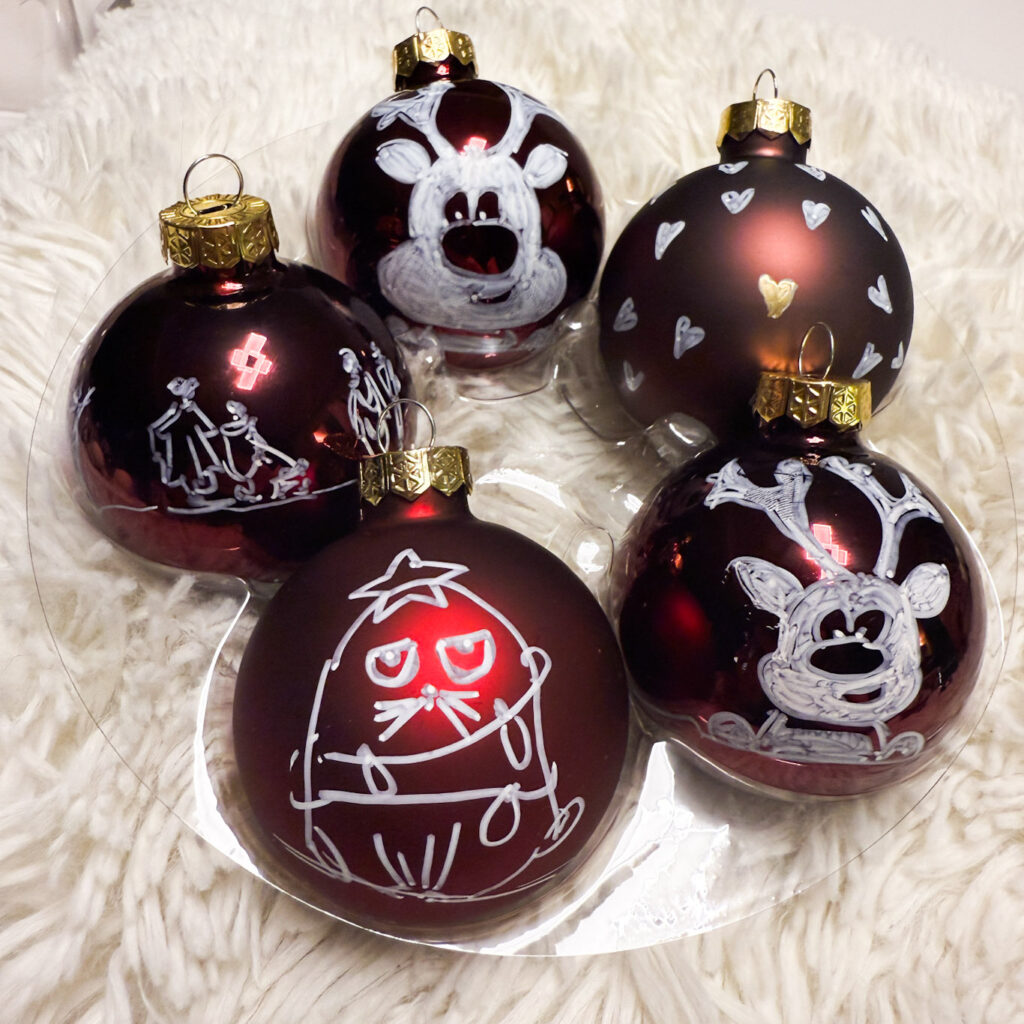 Symboles de Noël sur une boule de Noël en verre, création Atelier VADE.
boule rouge bordeaux brillante et mate, rennes, coeurs, Chat, personnages dessinés